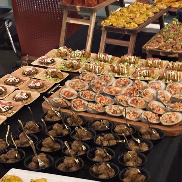 A buffet table with various Mexican appetizers, including taquitos, sopes, ceviche, and meatballs.