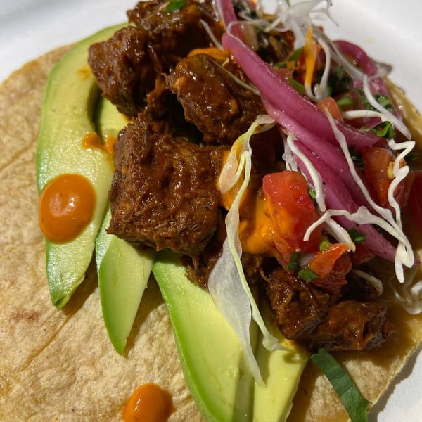 Close-up of a Rene's Mexican Kitchen taco with braised meat, avocado, pickled onions, and salsa.