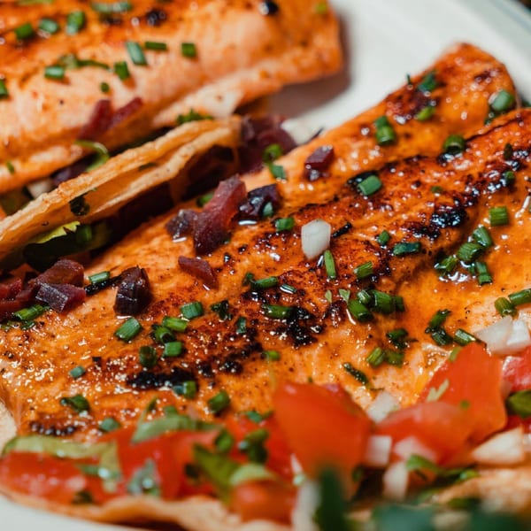 Close-up of two Rene's Mexican Kitchen tacos with grilled salmon, chives, and diced tomatoes.