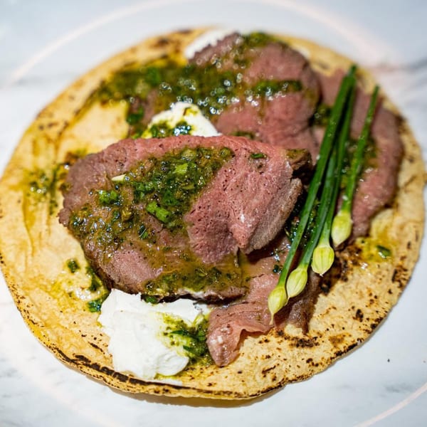 A Rene's Mexican Kitchen taco with sliced beef, green sauce, crema, and chive blossoms.