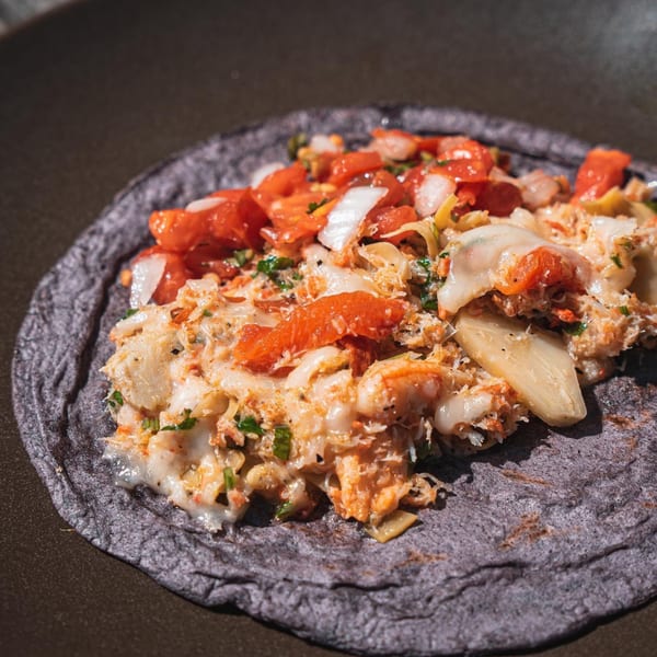 A close-up of a Rene's Mexican Kitchen blue corn tortilla taco filled with seafood and pico de gallo.