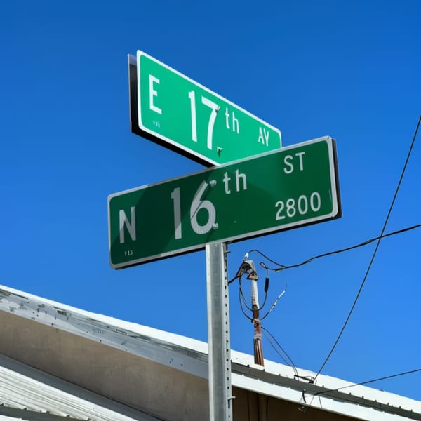 Green street signs for E 17th Ave and N 16th St against a clear blue sky.