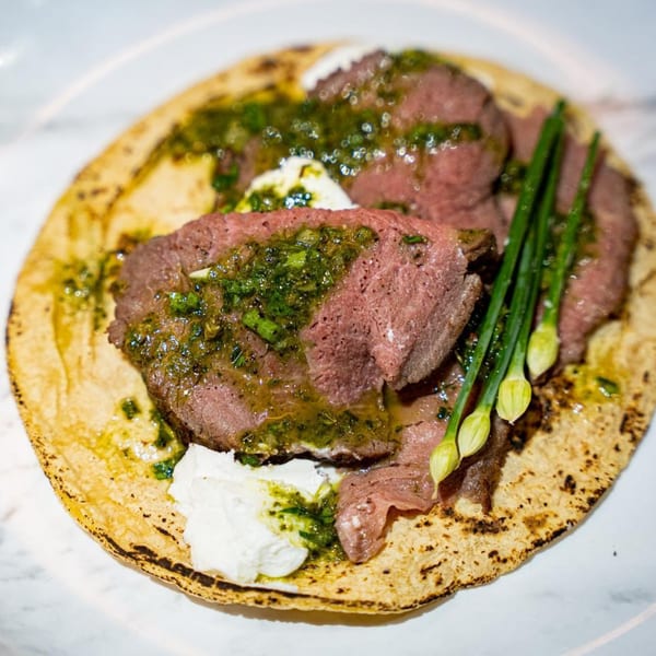 A Mexican taco with sliced beef, green sauce, white cream, and chives on a tortilla.