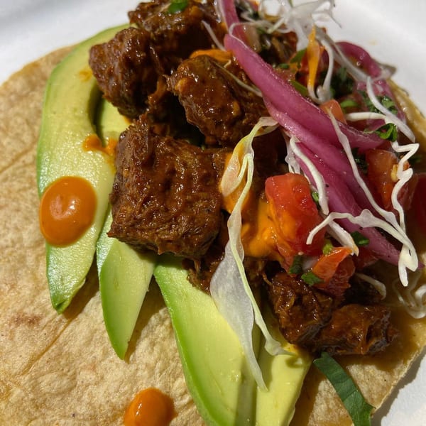 Close-up of a Rene's Mexican Kitchen taco with meat, avocado, red onion, and sauce.