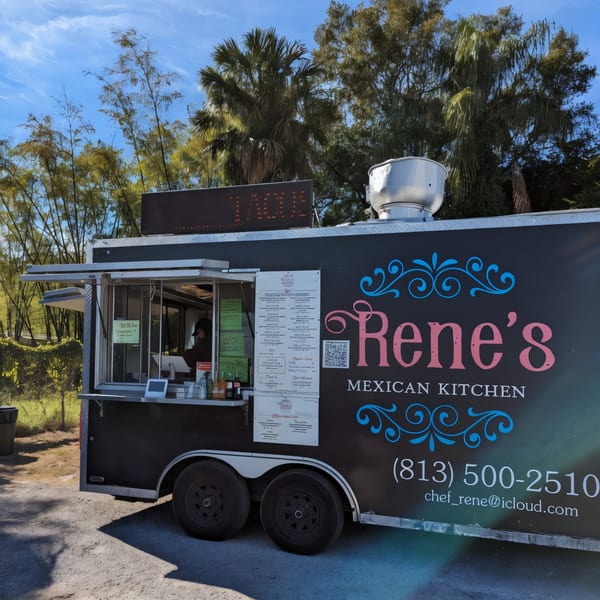Rene's Mexican Kitchen food truck, black with pink and blue lettering, parked outdoors under a blue sky.