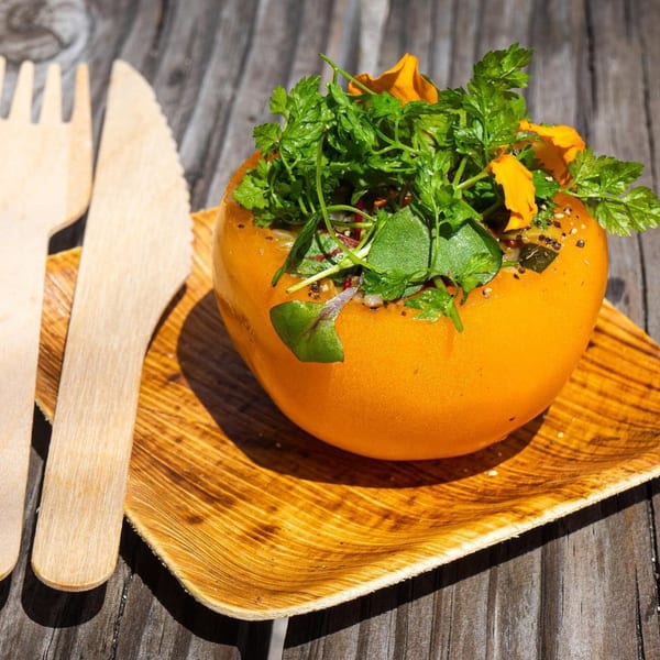 A vibrant orange stuffed bell pepper, garnished with fresh herbs and edible flowers, on a wooden plate.