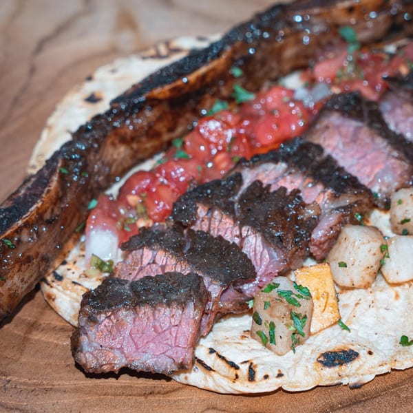 Grilled steak with salsa and potatoes on a tortilla, served on a wooden board.