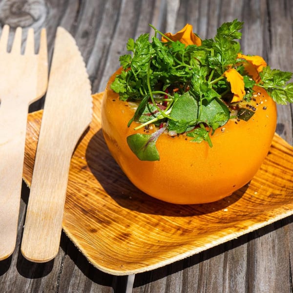 A vibrant orange bell pepper stuffed with fresh herbs and edible flowers, served on a wooden plate.